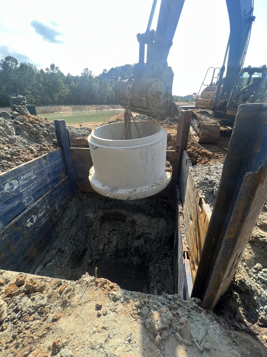 Excavators setting a precast pump station manhole in a deep trench